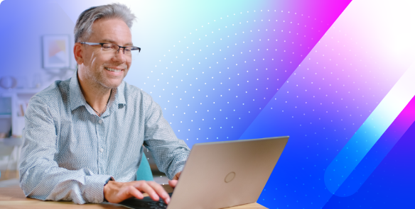 Man with glasses, buttoned up colored shirt, and gray hair smiles while working on a laptop at a desk