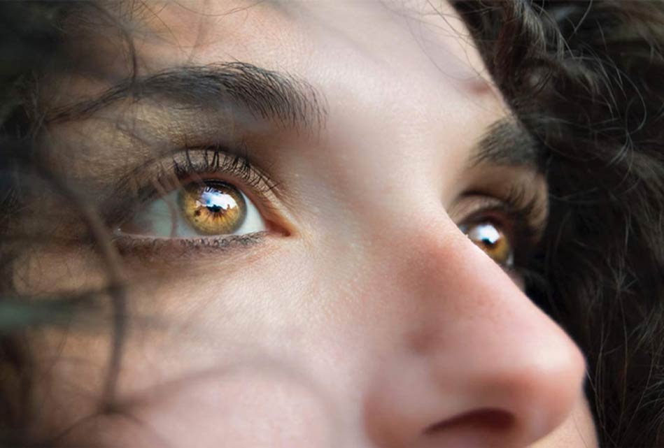 Close-up of a woman’s face with brilliant hazel eyes, looking upward with soft lighting
