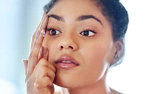 Close-up of a woman inserting a contact lens into her eye, using one hand to hold her eyelid open