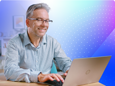 Smiling man wearing glasses working on a laptop in a brightly lit office or home workspace