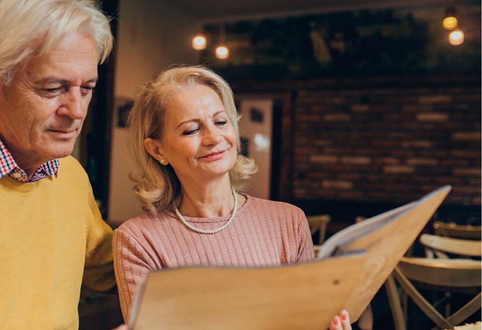 A middle-aged woman reading a book indoors without glasses, representing improved intermediate and near vision
