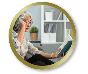 Older woman sitting on a couch reading a book while adjusting her glasses