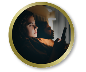 Woman in bed using her phone in low light, representing everyday visual comfort needs