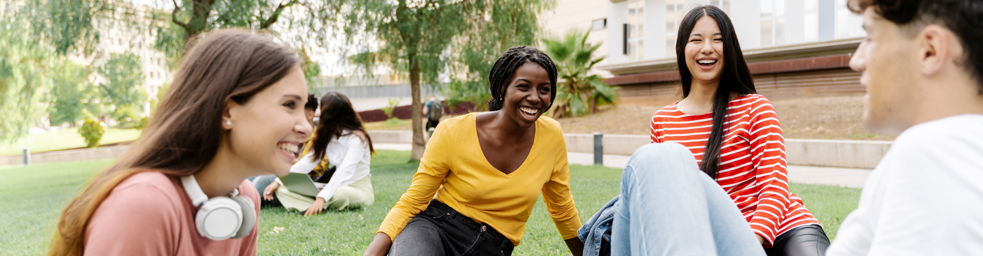 Group of students sitting on the grass outdoors, laughing and talking together on campus