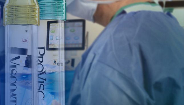 A close-up shot of two tubes of Alcon Ophthalmic Viscosurgical Devices. The tube with the yellow cap is labelled VISCOAT, and the tube with the green cap is labelled PROVISC. Behind the tubes there is a surgeon wearing a medical mask and surgical scrubs.